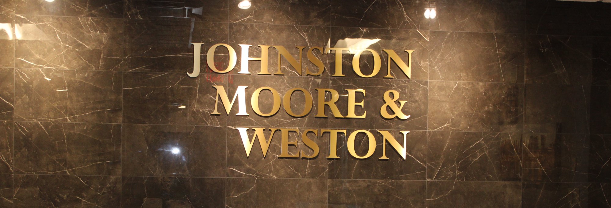 The Johnston, Moore & Weston reception wall — gold lettering on dark marble, Suite 200